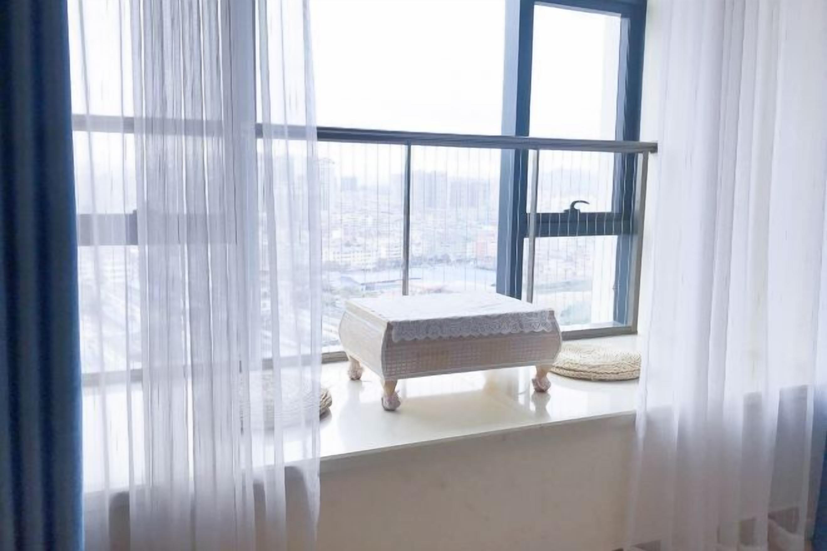 A room with a small white bench by a window with a view of a cityscape.