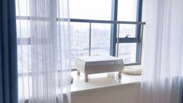 A room with a small white bench by a window with a view of a cityscape.