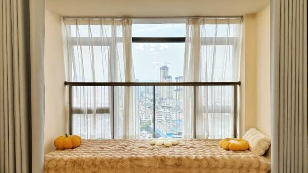 Ein Fensterplatz mit Blick auf eine Stadtlandschaft, eine gepolsterte Bank und zwei Kürbisse.