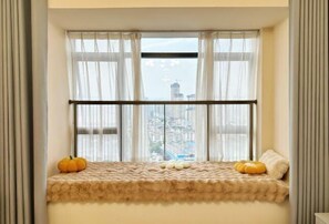 Asiento junto a la ventana con vista a un paisaje urbano, un banco acolchado y dos calabazas.