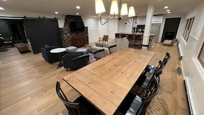 A spacious living area with a large wooden dining table, black chairs, a stone fireplace, and a modern kitchen in the background. - 4 Season Fun on Lake Namakagon - Snowmobiling, Boating, Fishing, UTV & More! (Cable)