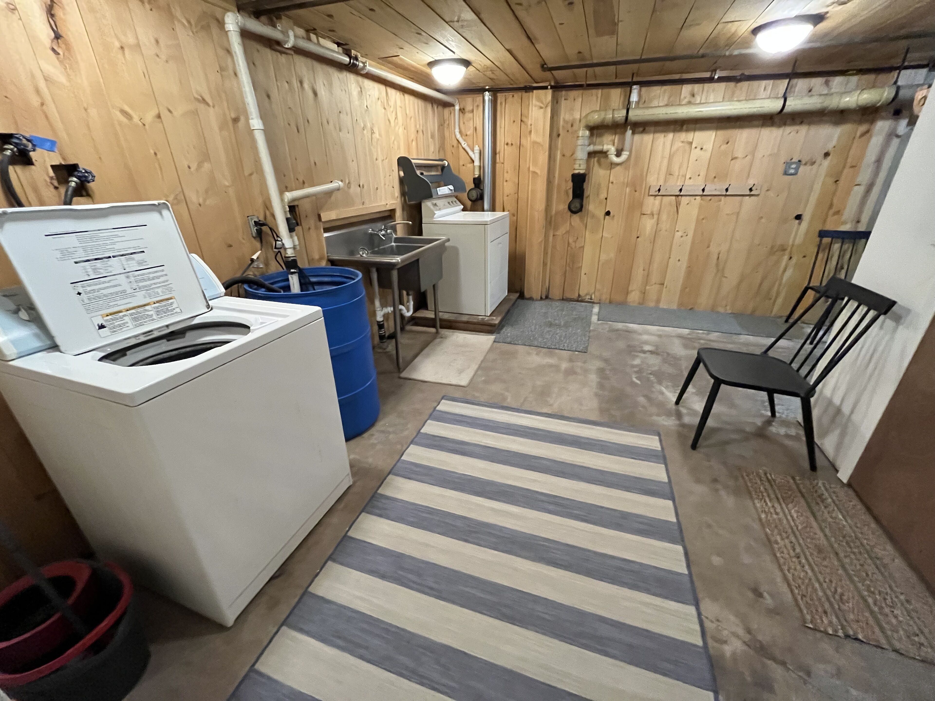 Une buanderie équipée d’un lave-linge, de barils bleus, d’un évier et d’une chaise.