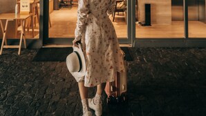A woman in a floral dress and white hat standing at a doorway, holding a suitcase. - VOQUE Hotel & Serviced Residence Sukhumvit 51 (Bangkok)
