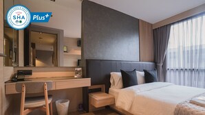 A hotel room with a bed, a desk, a chair, a trash bin, and a large window with curtains. - VOQUE Hotel & Serviced Residence Sukhumvit 51 (Bangkok)