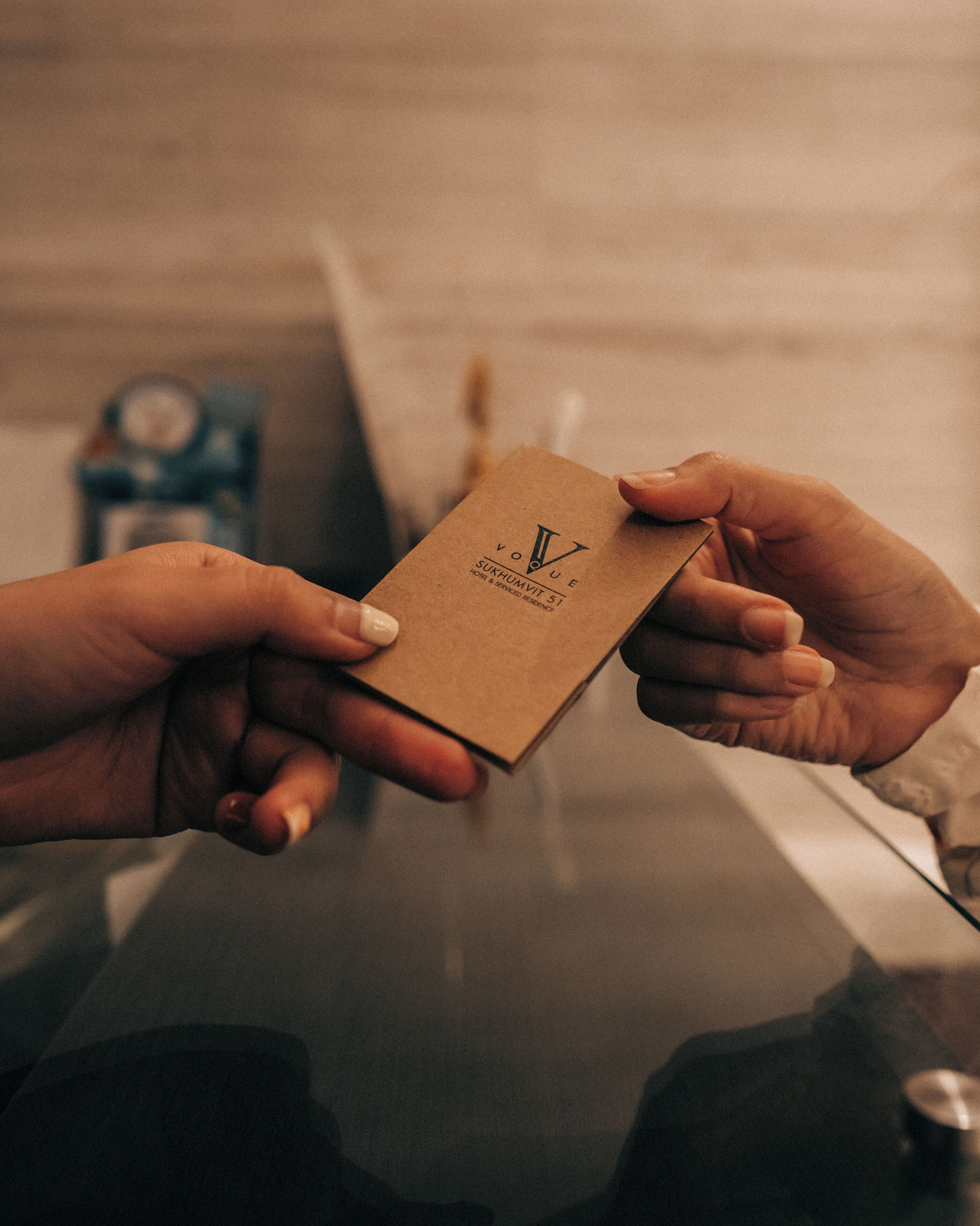 A person holding a brown card with the text "Vogue Sukhumvit St."