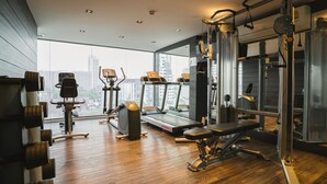 A modern gym with exercise equipment, a treadmill, and a view of the city through large windows. - VOQUE Hotel & Serviced Residence Sukhumvit 51 (Bangkok)