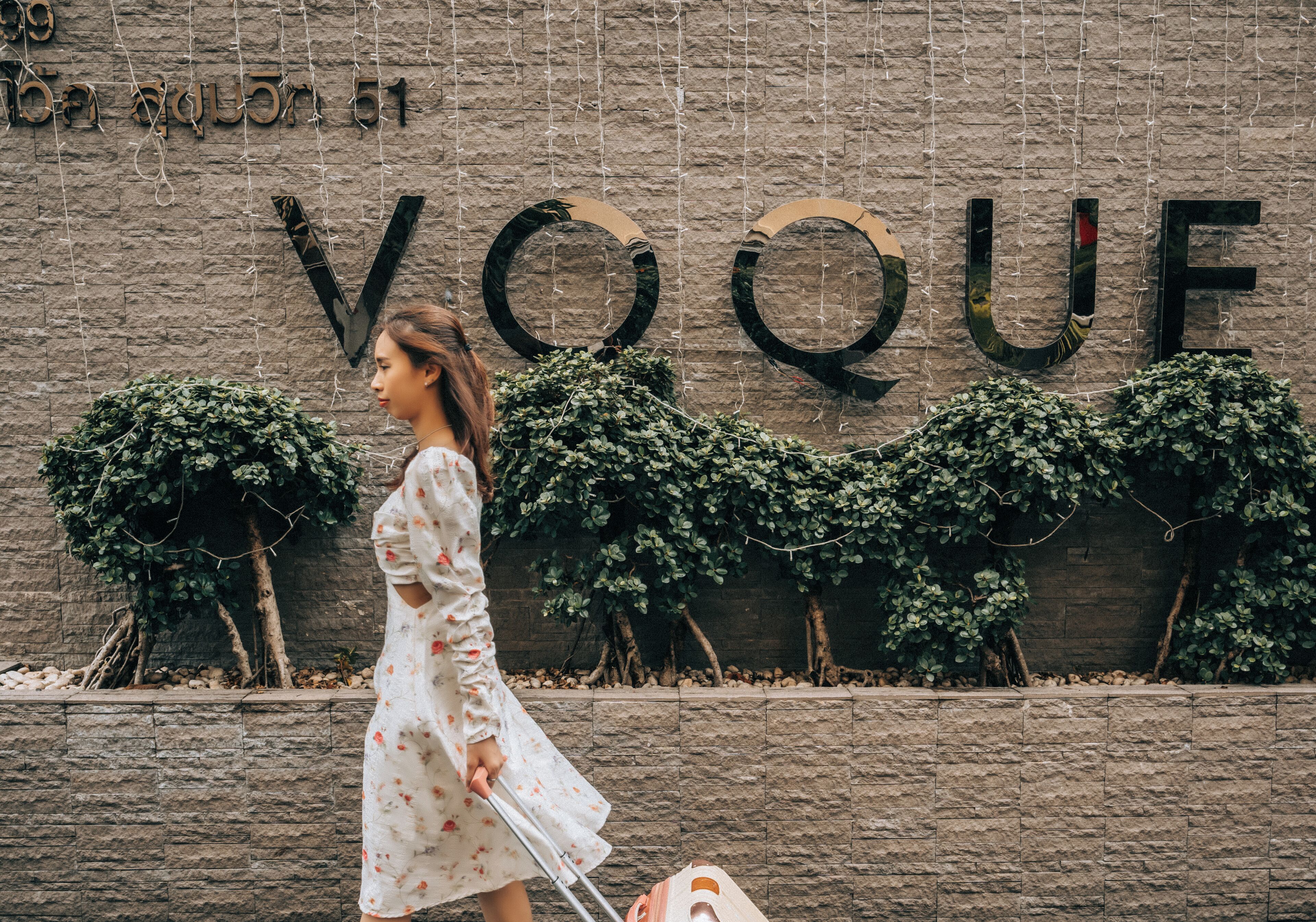 A woman in a white dress walking past a wall with the word "VOGUE" in large letters.