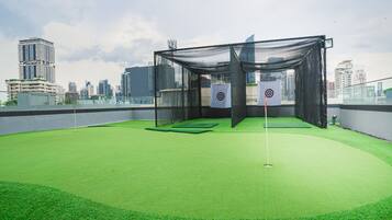 Un espai de pràctica de golf amb gespa a la terrassa, delimitat per una xarxa, envoltat d'edificis alts.