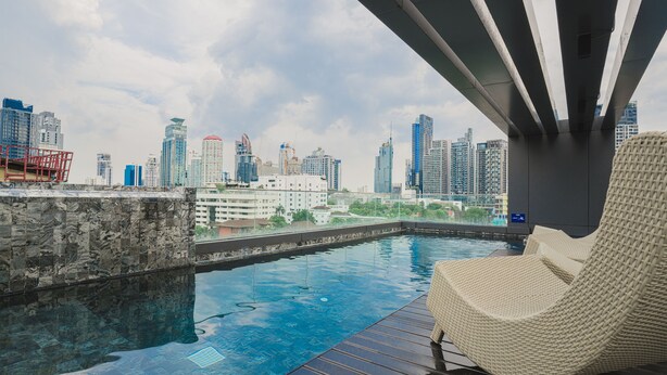 A rooftop infinity pool with a city skyline view, a wicker lounge chair, and a modern architectural design. - VOQUE Hotel & Serviced Residence Sukhumvit 51 (Bangkok)