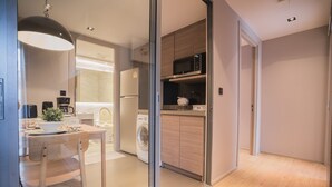 A modern kitchen with a washing machine, microwave, and a dining area with a table and chairs. - VOQUE Hotel & Serviced Residence Sukhumvit 51 (Bangkok)