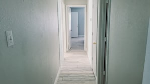 Kapea käytävä, jonka seinät ovat valkoiset ja lattia puuta, johtaa käytävän päässä olevaan oveen.