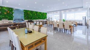 Un comedor amplio con varias mesas y sillas, una pared verde con diseño inspirado en la naturaleza, y un interior luminoso y bien iluminado.
