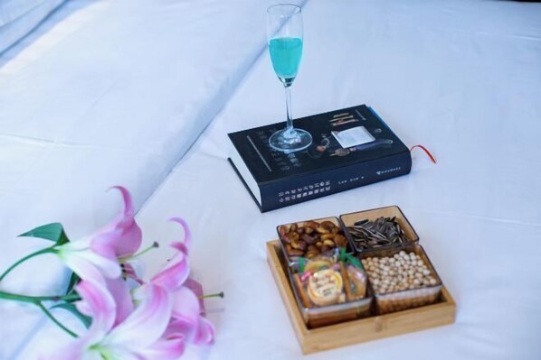 A table with a glass of blue liquid, a black electronic device, and a wooden box containing various snacks and nuts. - Ninglang Lugu Lake Hotel (Ninglang)