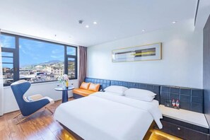 A hotel room with a large bed, a seating area, a small table, and a view of the city.