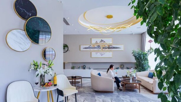Un interior moderno con suelo de mármol, una mujer sentada en un sofá y una mesa con flores.