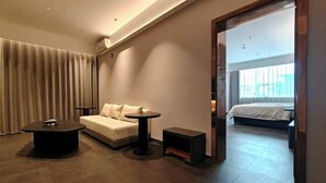 Ett modernt hotellrum med en soffa, två små bord, en säng och ett stort fönster.