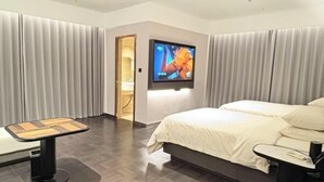Ett modernt hotellrum med en stor säng, en platt-TV som är monterad på väggen, ett litet bord och en dörr som leder till badrummet.