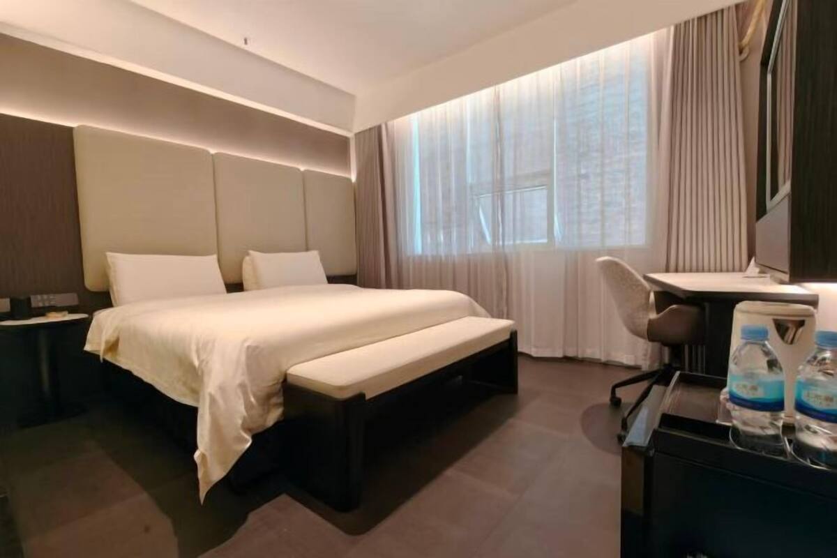 Una habitación de hotel con cama, escritorio, silla, banco y dispensador de agua.