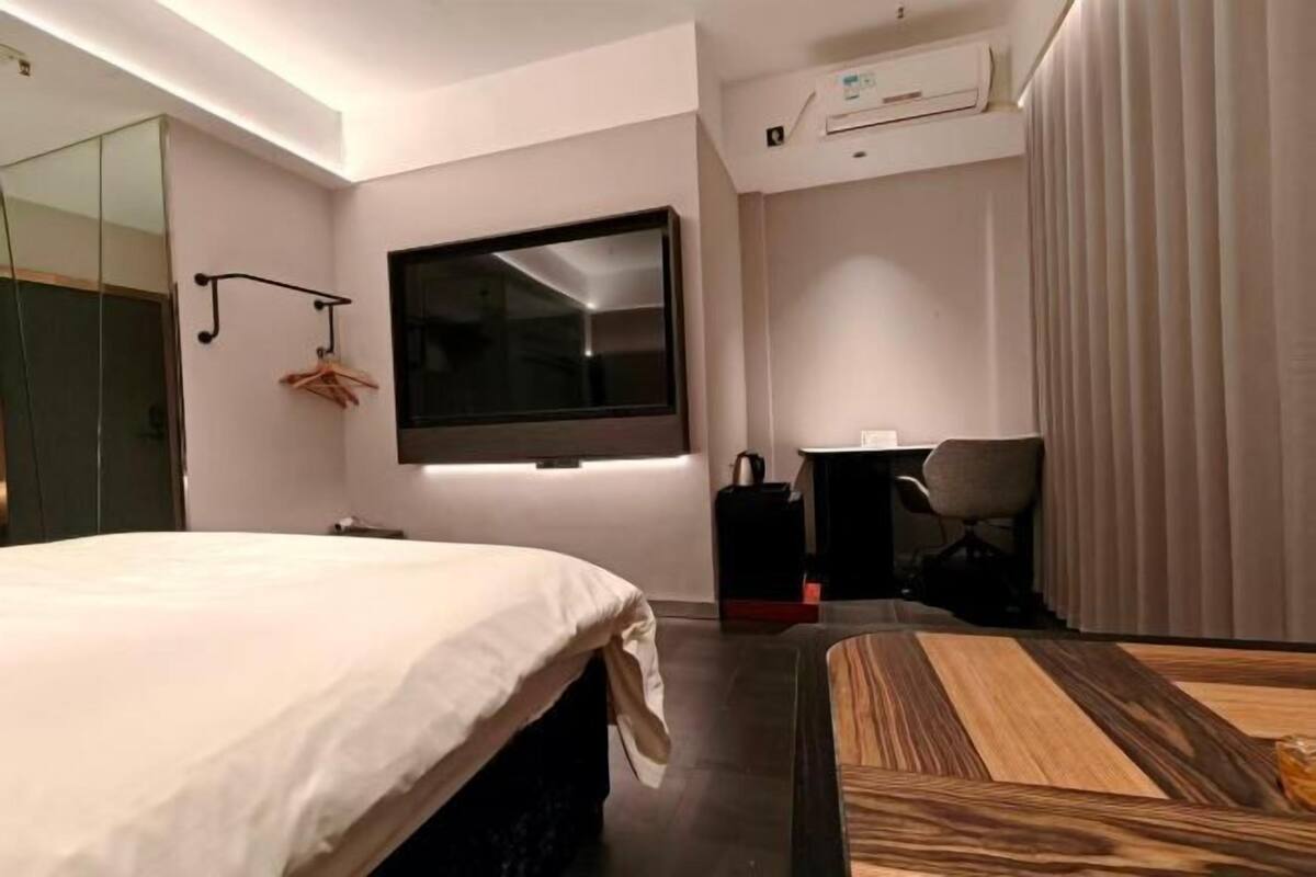 Habitación de hotel con cama, escritorio, silla, televisor y espejo.