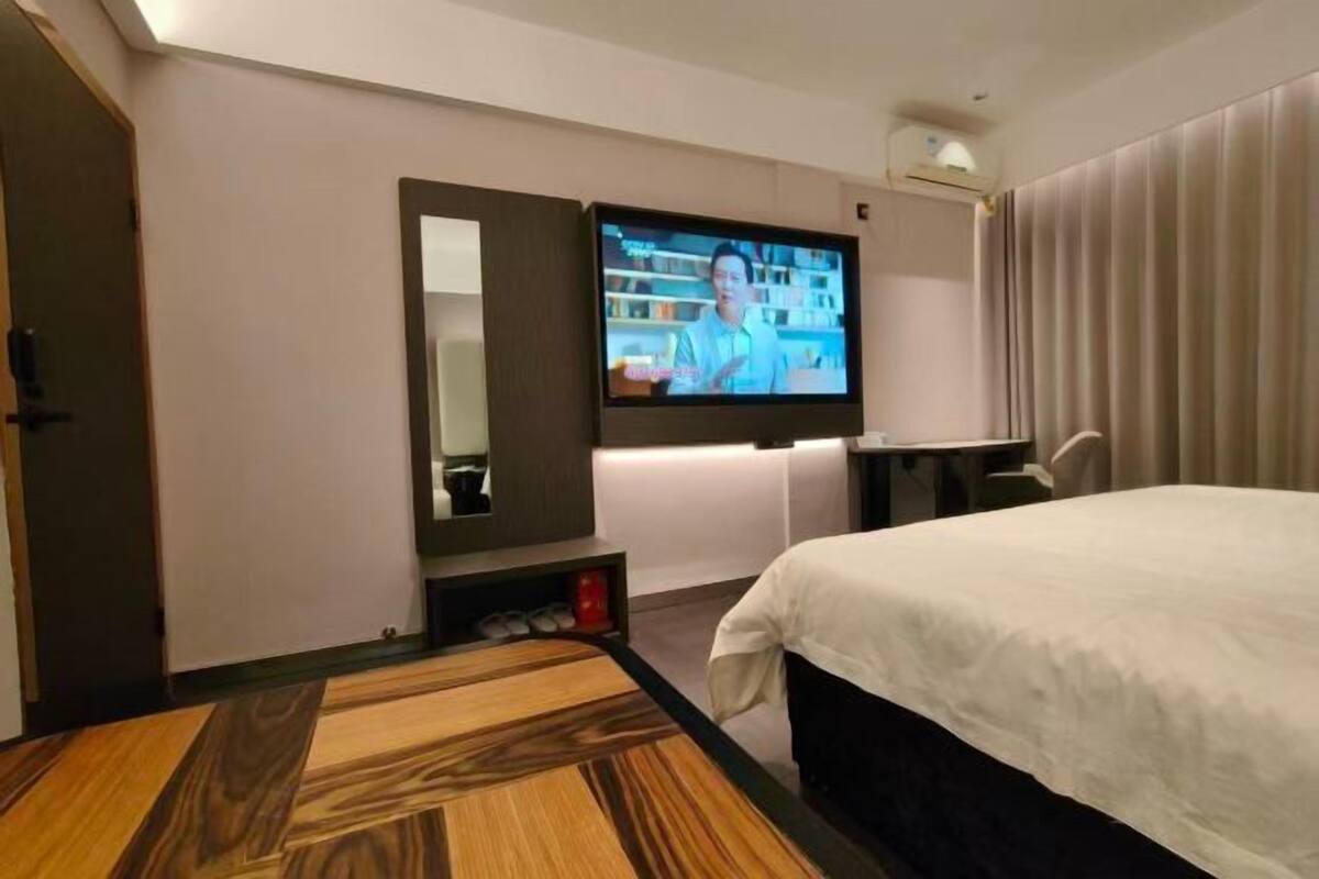 Habitación de hotel con cama, televisor montado en la pared, una mesita y un espejo.