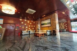 A lobby with a marble floor, a reception desk, a seating area with sofas, and a wall with a painting. - Jin Ting Hotel (Shanglin)