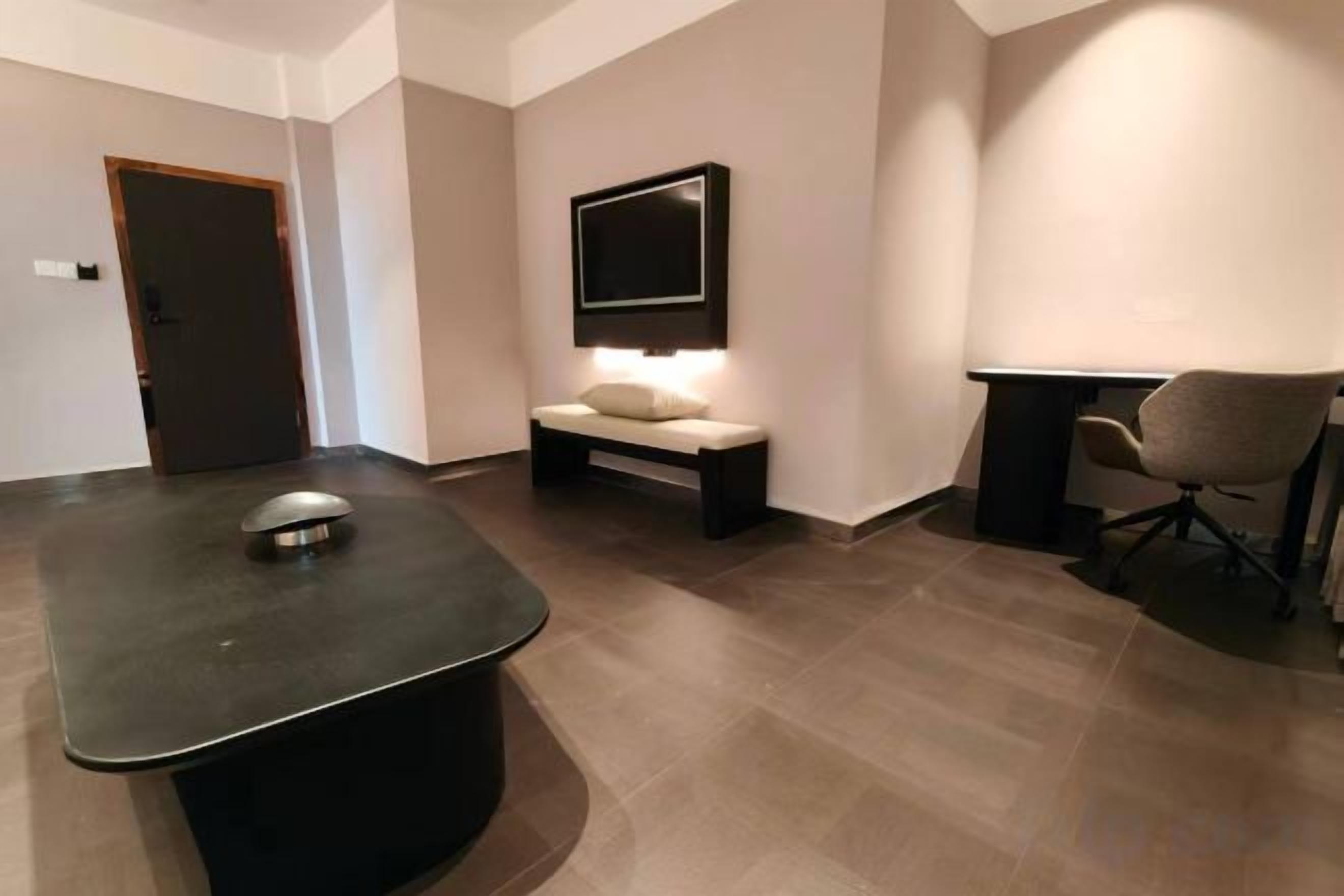 A room with a massage table, a bench, a TV mounted on the wall, and a chair.