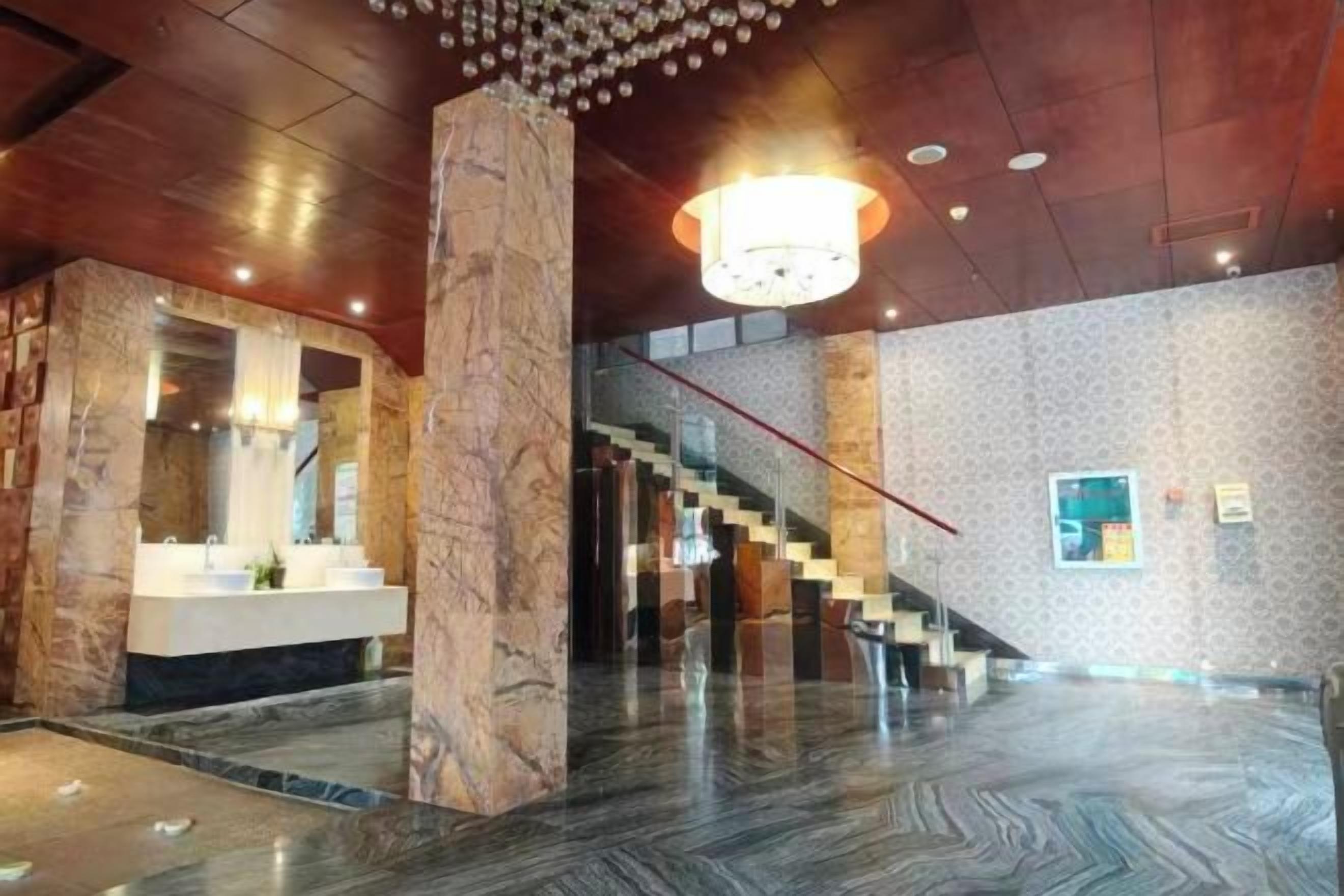 A spacious lobby with a marble column, a staircase, and a modern chandelier.