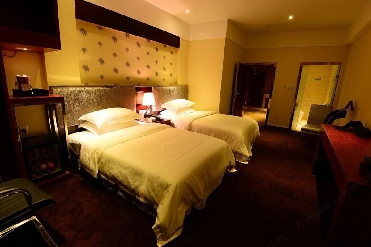 A hotel room with two beds, a nightstand, a lamp, and a small table with a chair.