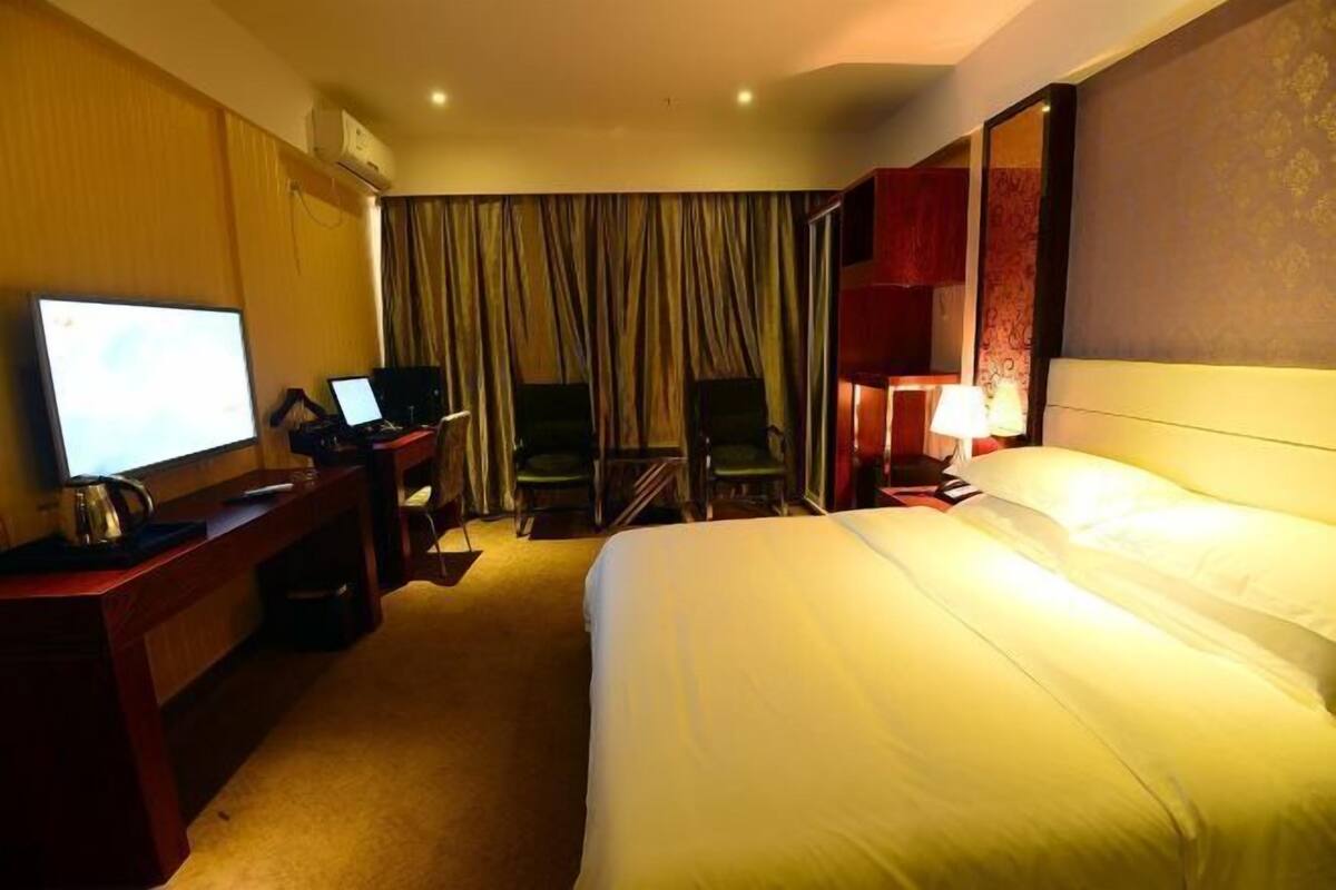 Una habitación de hotel con una cama, un escritorio con una computadora portátil, un televisor y una silla.