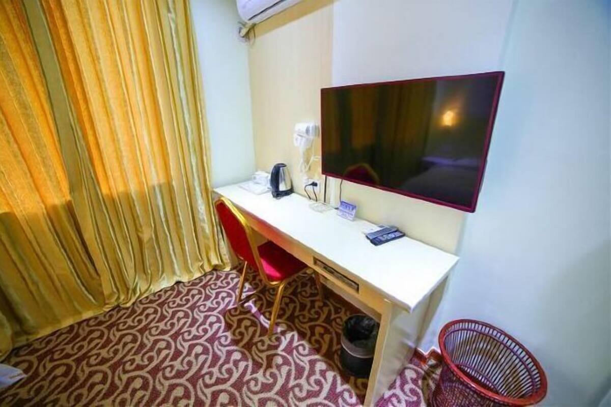 Habitación de hotel con escritorio blanco, televisión de pantalla plana, silla roja, alfombra estampada y basurero rojo.