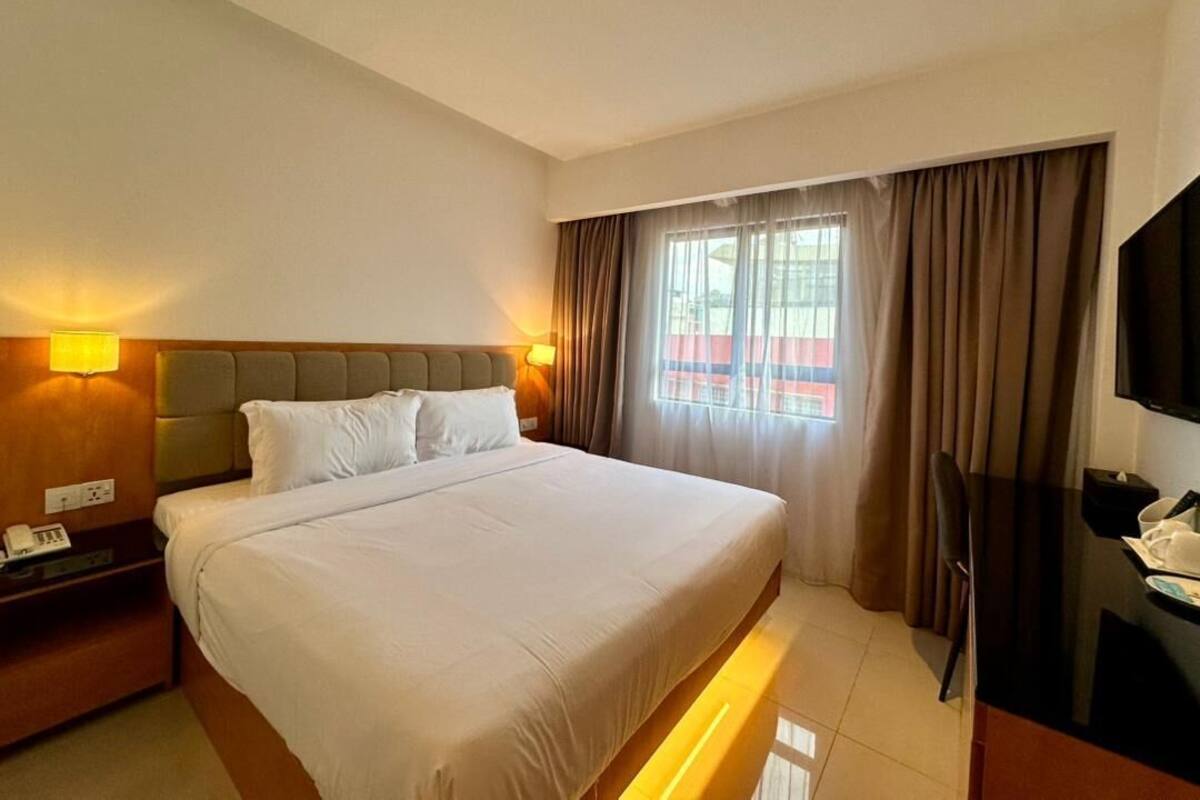 A hotel room with a large bed, bedside lamps, a television, and a window with curtains.