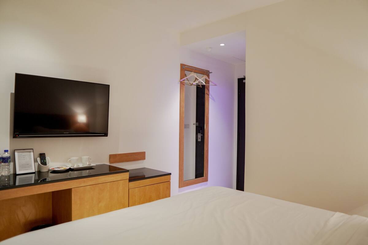 A hotel room with a bed, a TV mounted on the wall, a wooden dresser, and a mirror.