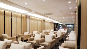 A modern lounge area with rows of beige sofas and armchairs, a glass partition, and a staircase in the background. - D Loft Hotel (Kuala Lumpur)