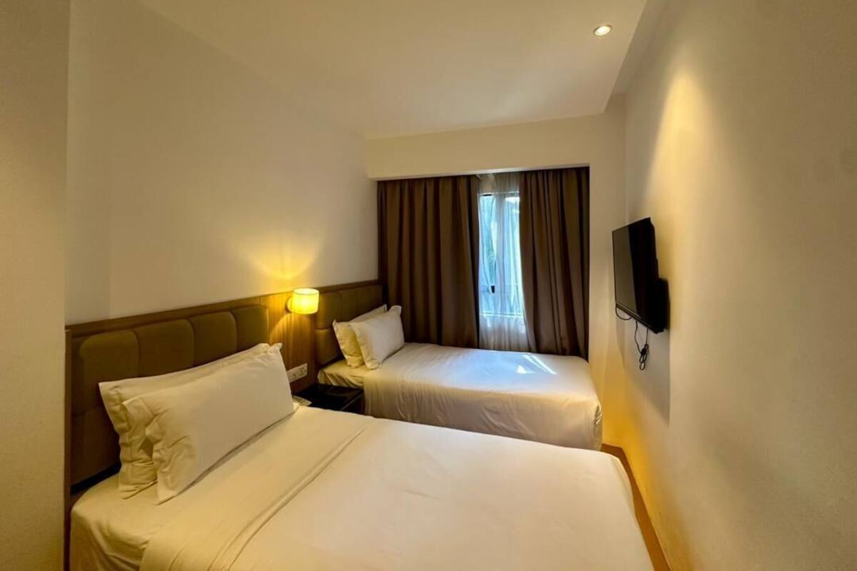 A hotel room with two beds, a TV mounted on the wall, and a window with curtains.