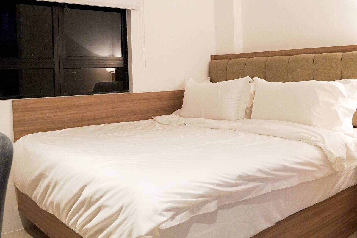 A modern bedroom with a wooden bed frame, white bedding, and a flat-screen TV mounted on the wall.