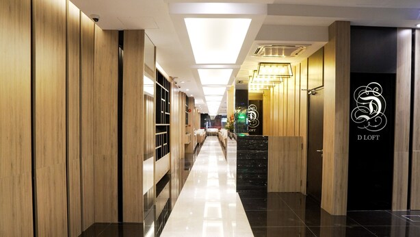A modern hotel corridor with wooden paneling, a black and white checkered floor, and a staircase leading to a room with a 'D LOFT' sign. - D Loft Hotel (Kuala Lumpur)