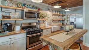 A modern kitchen with wooden countertops, stainless steel appliances, and a wooden island with stools. - Cozy Tybee Getaway on Butler Ave (Tybee Island)