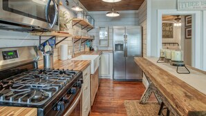 A modern kitchen with a gas stove, stainless steel appliances, wooden shelves, and a wooden countertop. - Cozy Tybee Getaway on Butler Ave (Tybee Island)