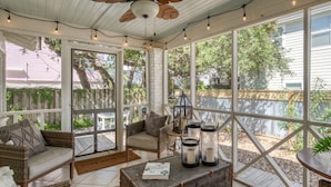 A covered porch with wicker furniture, a ceiling fan, string lights, and large windows. - Cozy Tybee Getaway on Butler Ave (Tybee Island)
