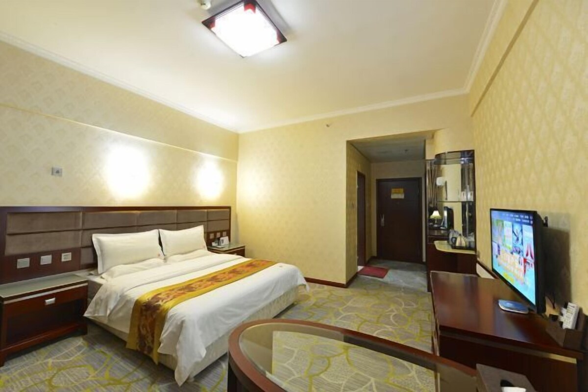 Habitación de hotel con cama, mesitas de noche, escritorio con computadora y televisión.