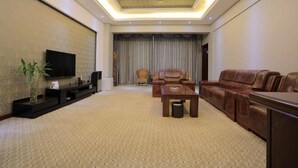 A modern living room with a flat-screen TV, leather sofas, a coffee table, and a large window with curtains.