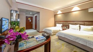 A hotel room with a bed, a desk with a computer, and a small table with flowers.