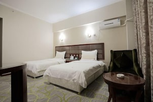 Habitación de hotel con dos camas, una mesita, una silla y un equipo de aire acondicionado en la pared.