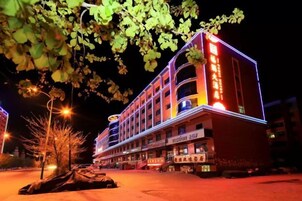 Un hotel de varios pisos con un cartel llamativo, una entrada bien iluminada y un área de estacionamiento.