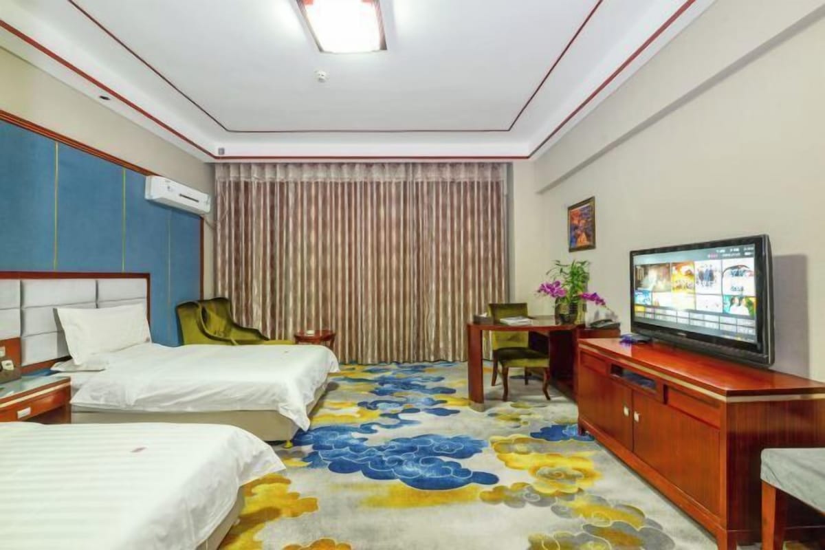 Habitación de hotel con dos camas, televisión, escritorio y una silla.