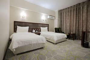 Ein Hotelzimmer mit zwei Betten, einem Nachttisch, einem Sessel und einem großen Fenster mit Vorhängen.