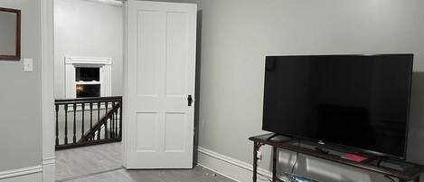 Una sala de estar con una televisión sobre un mueble de madera, una mesa de vidrio y una escalera que lleva a otra habitación.