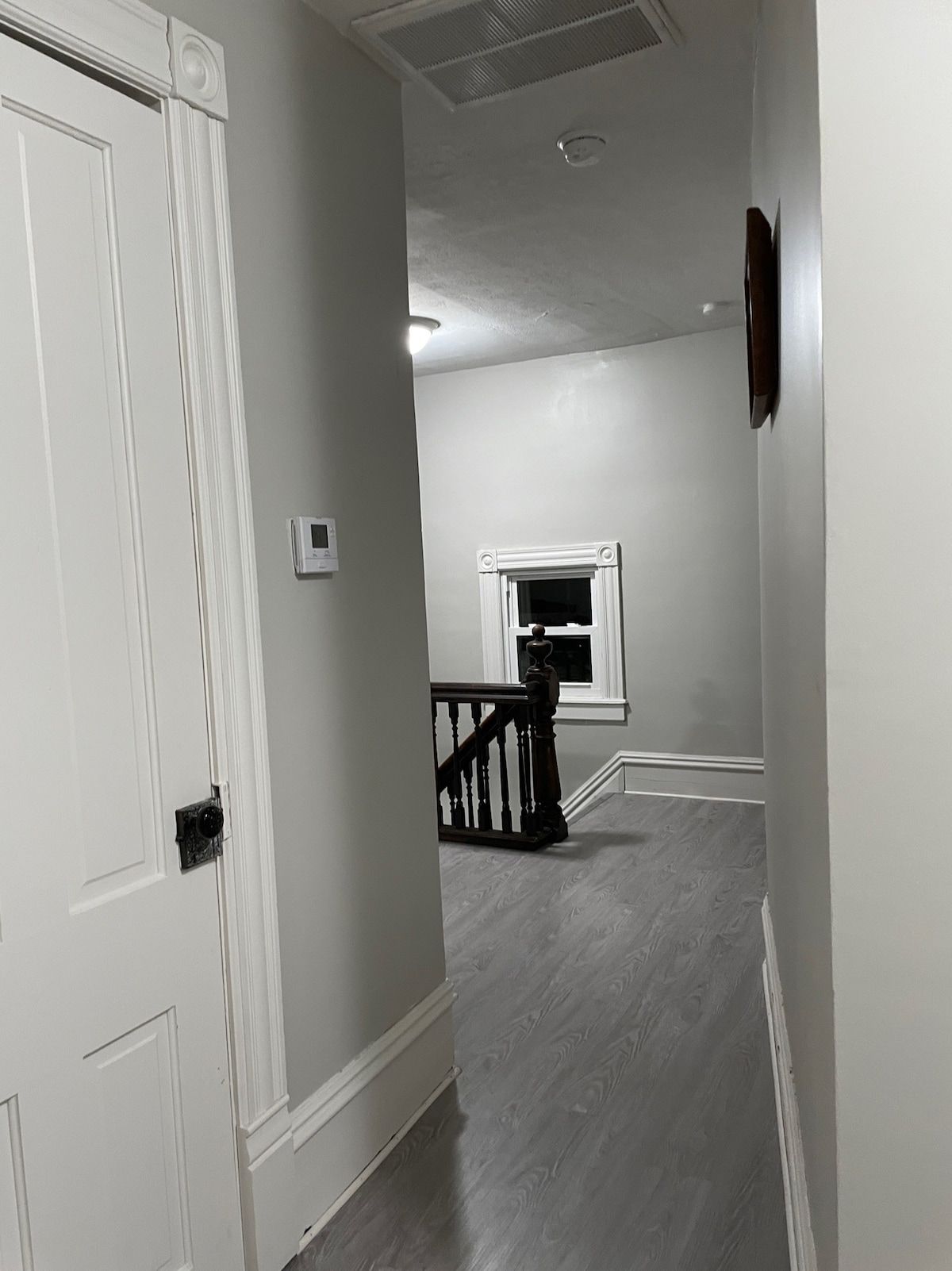 A hallway with a white door, a small window, and a staircase with a wooden railing.