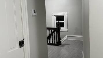 A hallway with a white door, a small window, and a staircase with a wooden railing.