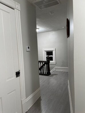 A hallway with a white door, a small window, and a staircase with a wooden railing.